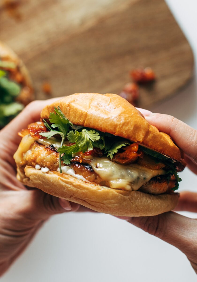 White hands holding chicken burgers with toppings
