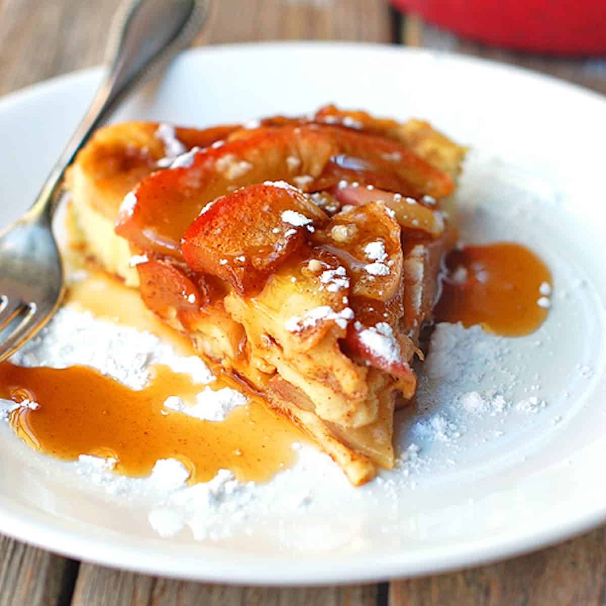 Baked apple pancake is baked in a cast iron skillet and topped with a homemade apple cider syrup on a white plate.